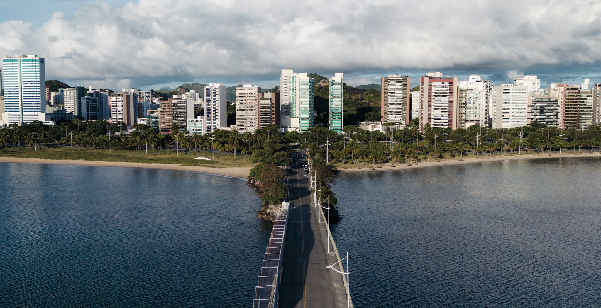 A bridge surrounded on both sides by water, headed into a city with a tree-covered coastline.