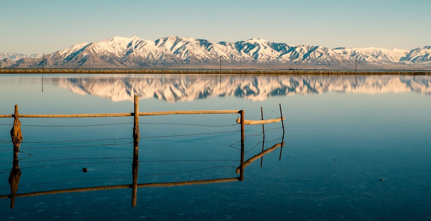 A small wooden fence in a vast lake with mountains in the background.