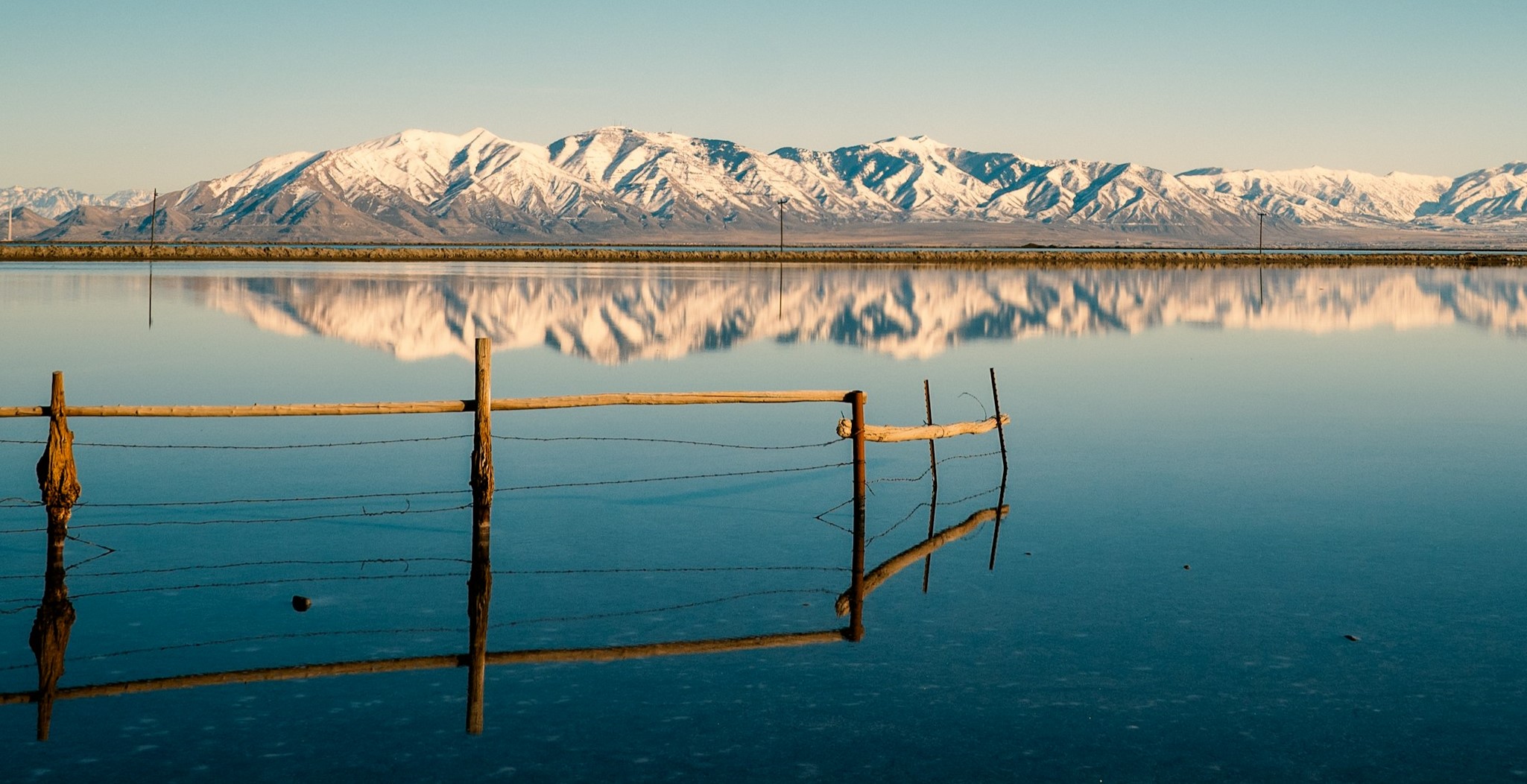 A small wooden fence in a vast lake with mountains in the background.