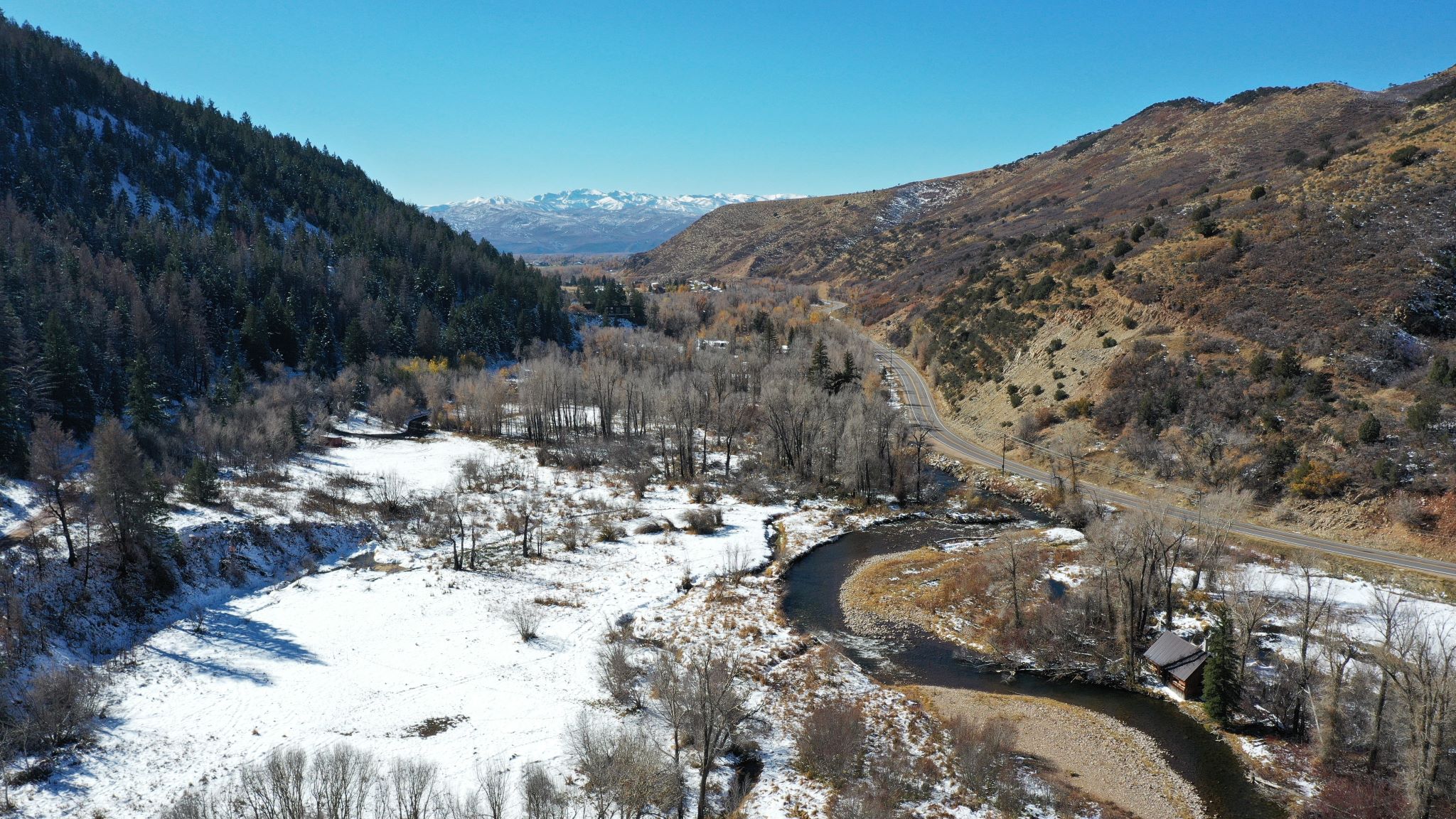 A river running alongside a snowy bank with two mountain peaks in the background.